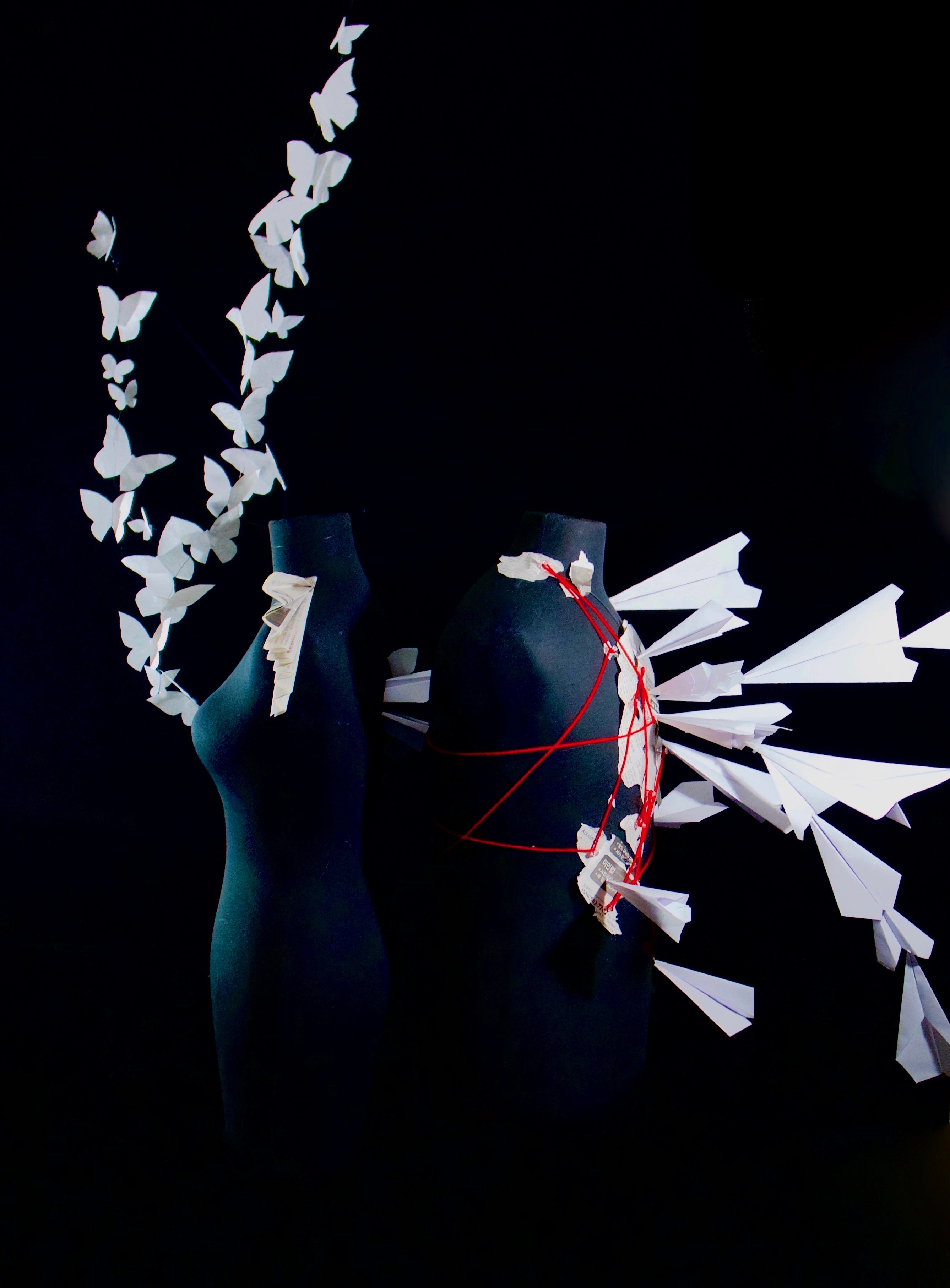 Two dark mannequins surrounded by radiating folded paper, yarn, and wire.